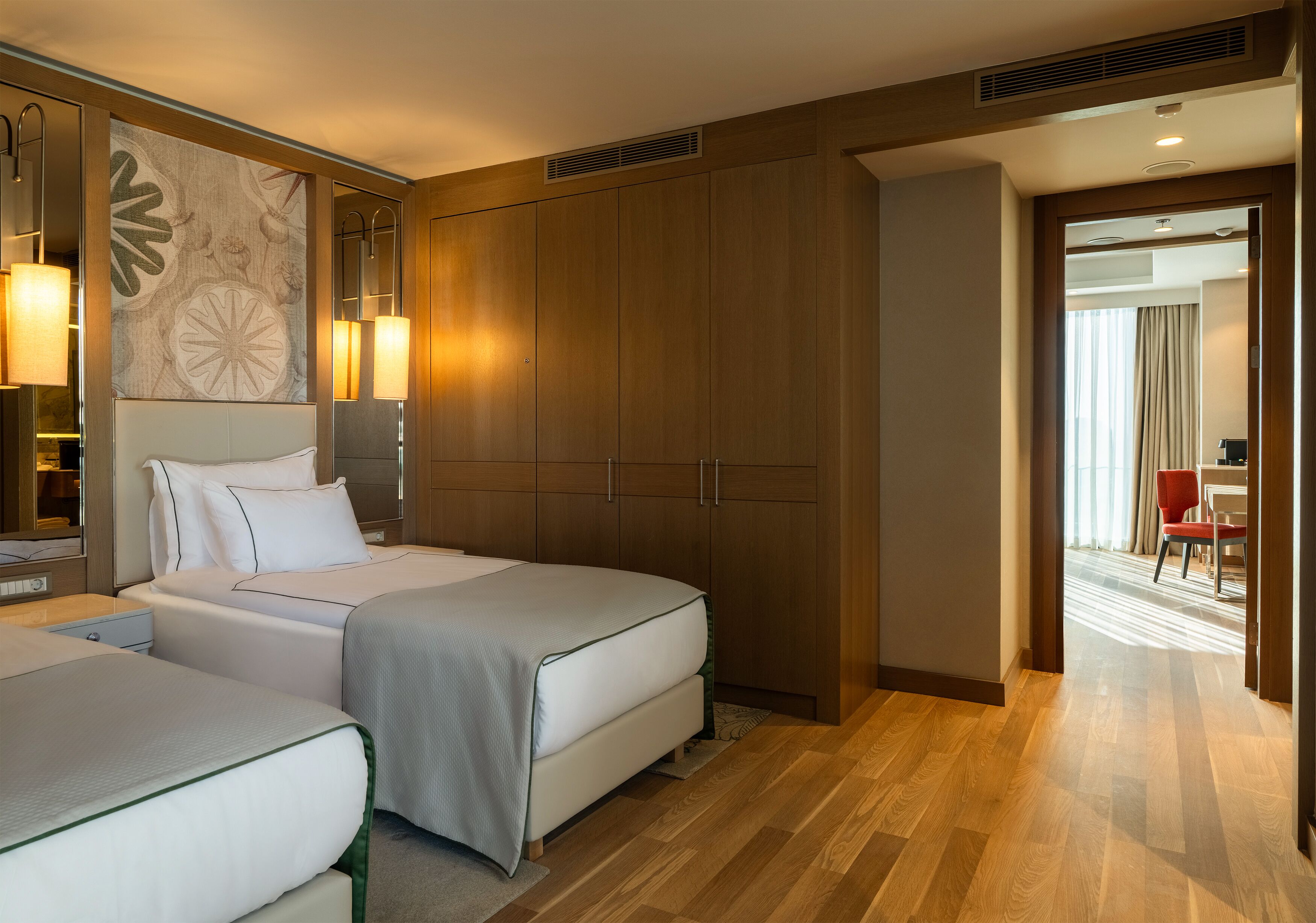 Habitación de hotel con dos camas, un armario grande, un escritorio y vista al pasillo.
