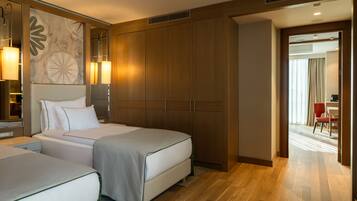 Habitación de hotel con dos camas, un armario grande, un escritorio y vista al pasillo.