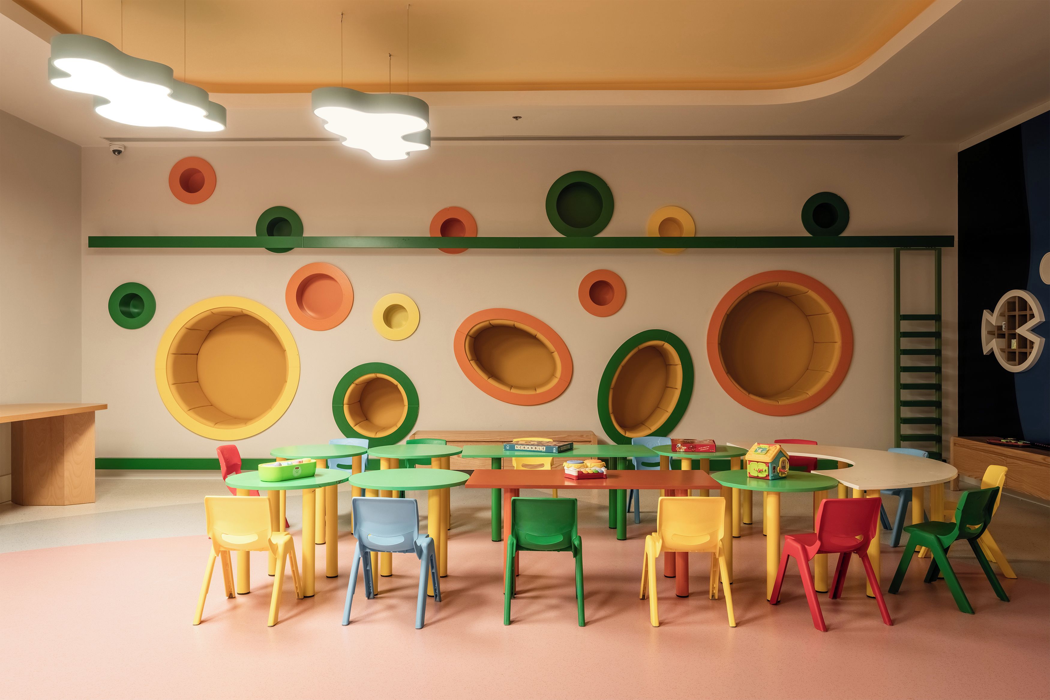 Una sala de juegos infantil con coloridos adornos circulares en las paredes, diversas mesas y sillas pequeñas, y una lámpara en el techo.