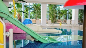 An indoor pool area with a water slide, lounge chairs, and palm trees. - Sinnada Resort & Thermaland (Afyonkarahisar)