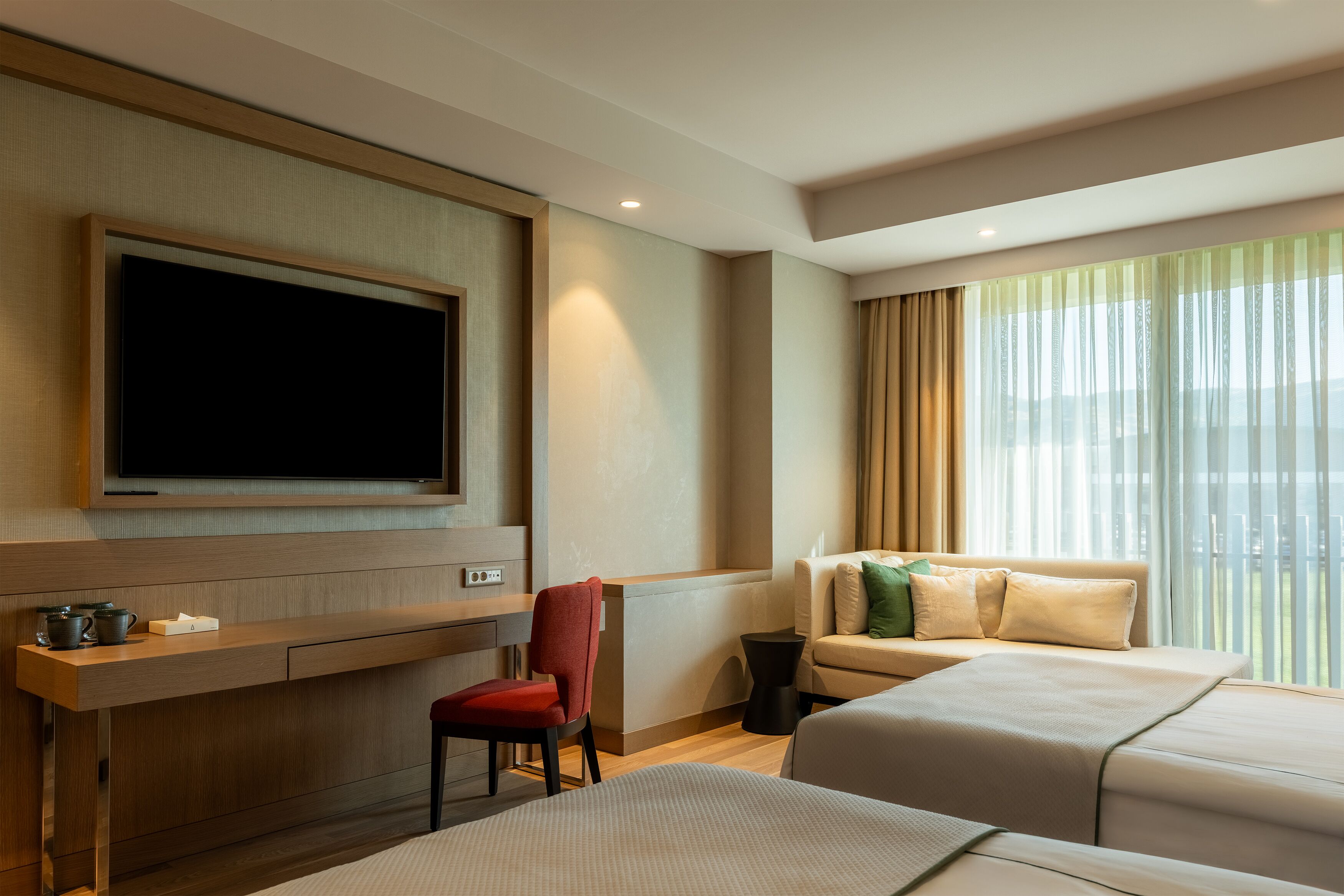 Habitación de hotel con televisión de pantalla plana montada en la pared, un escritorio con silla, un sofá y una cama.