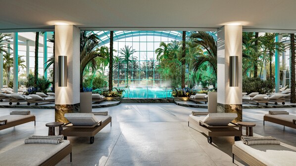 Un área de piscina interior moderna con sillones de descanso, vista despejada de la piscina y plantas tropicales.