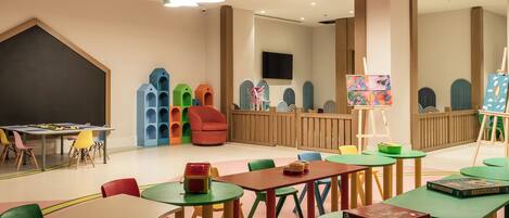 A children's playroom with colorful furniture, a blackboard, and a painting on easel.