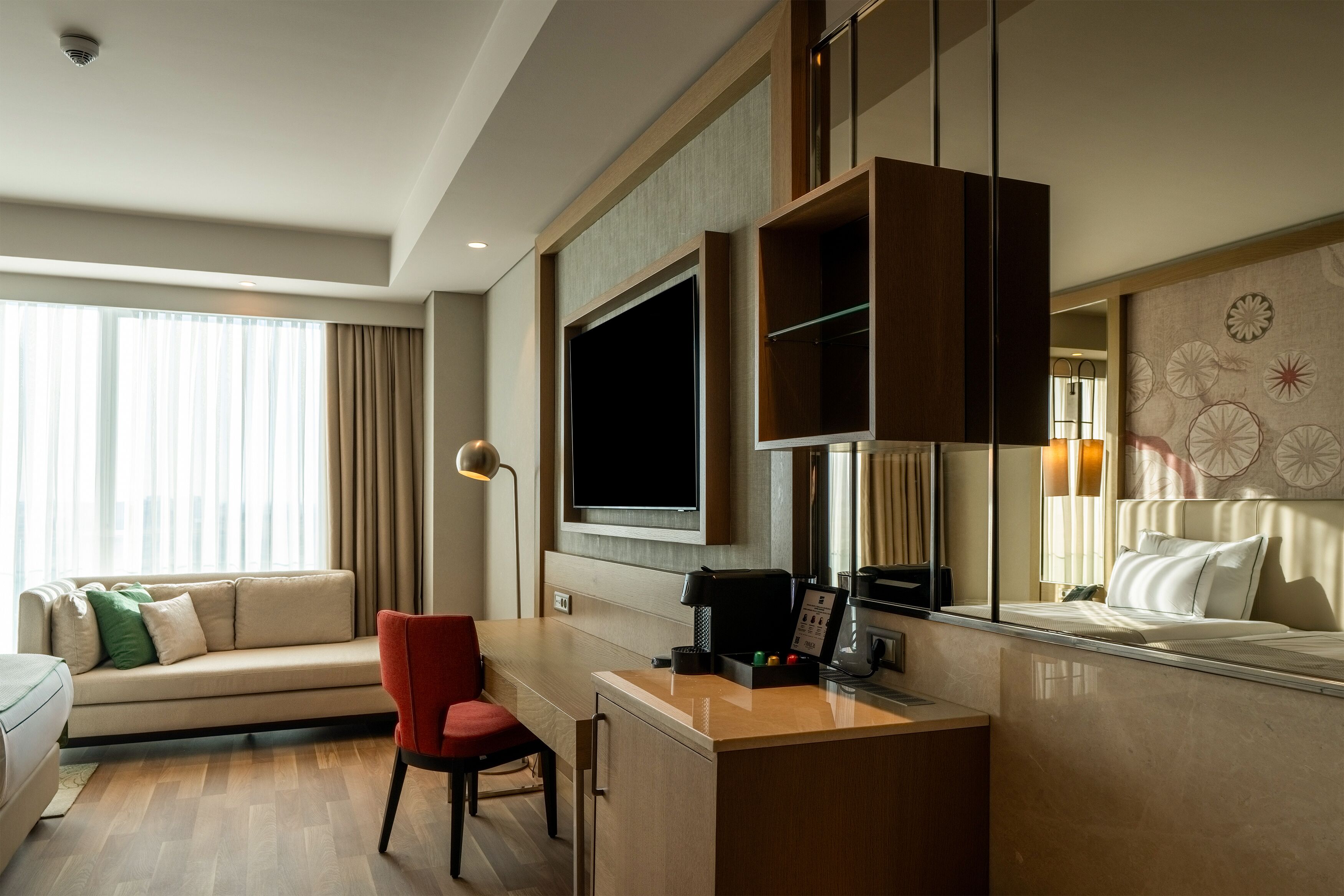Ein Hotelzimmer mit Sofa, Schreibtisch mit Stuhl, Flachbildfernseher, einer Kaffeemaschine und einem Bett mit Kopfteil.
