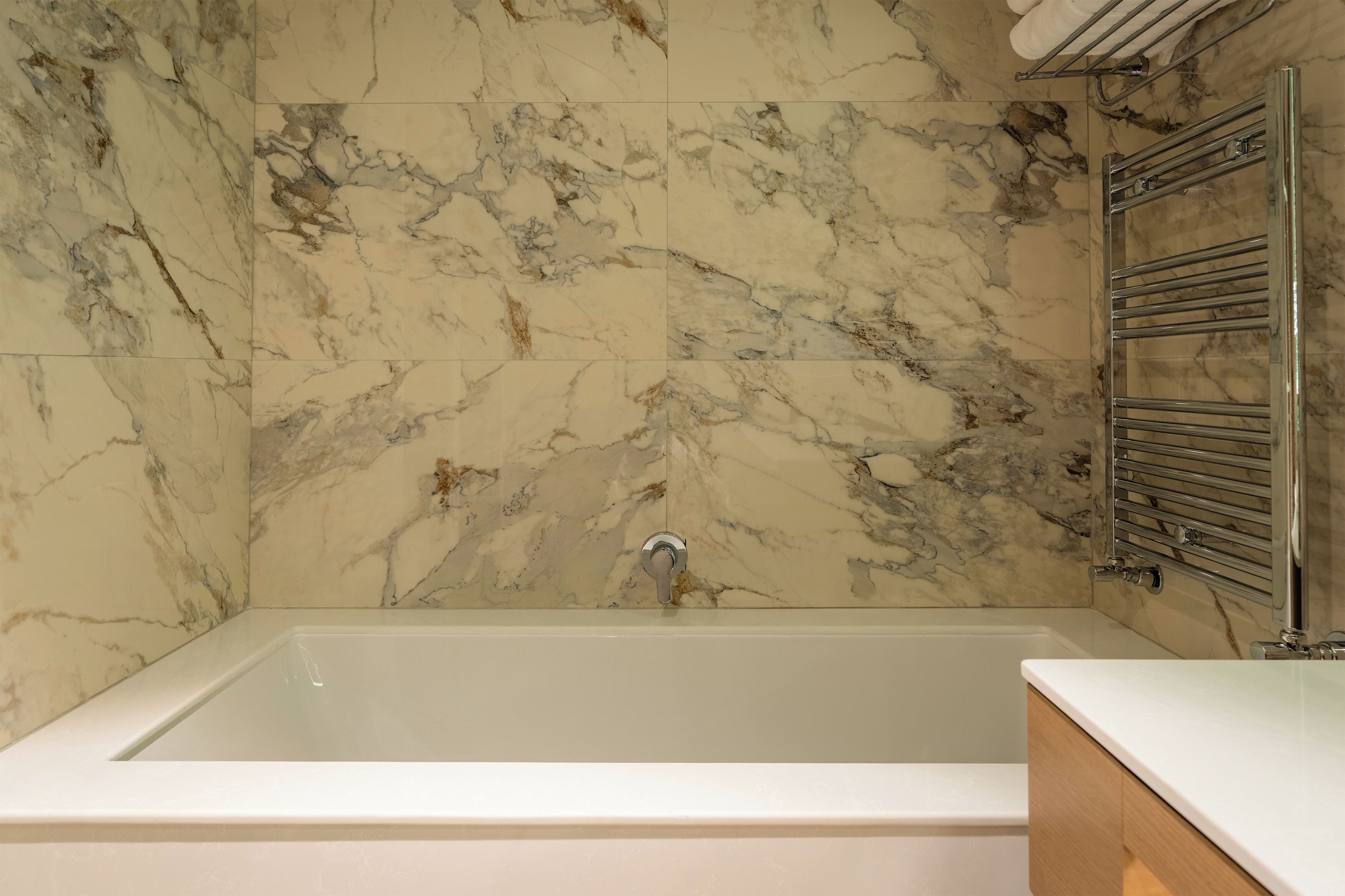 Un baño con pared de mármol, una bañera y un toallero cromado.