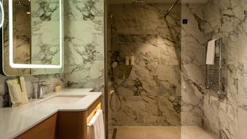 A modern bathroom with a marble shower, a large mirror, and a vanity with toiletries.