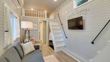 A cozy living room with a gray sofa, a white staircase, and a flat-screen TV mounted on the wall.