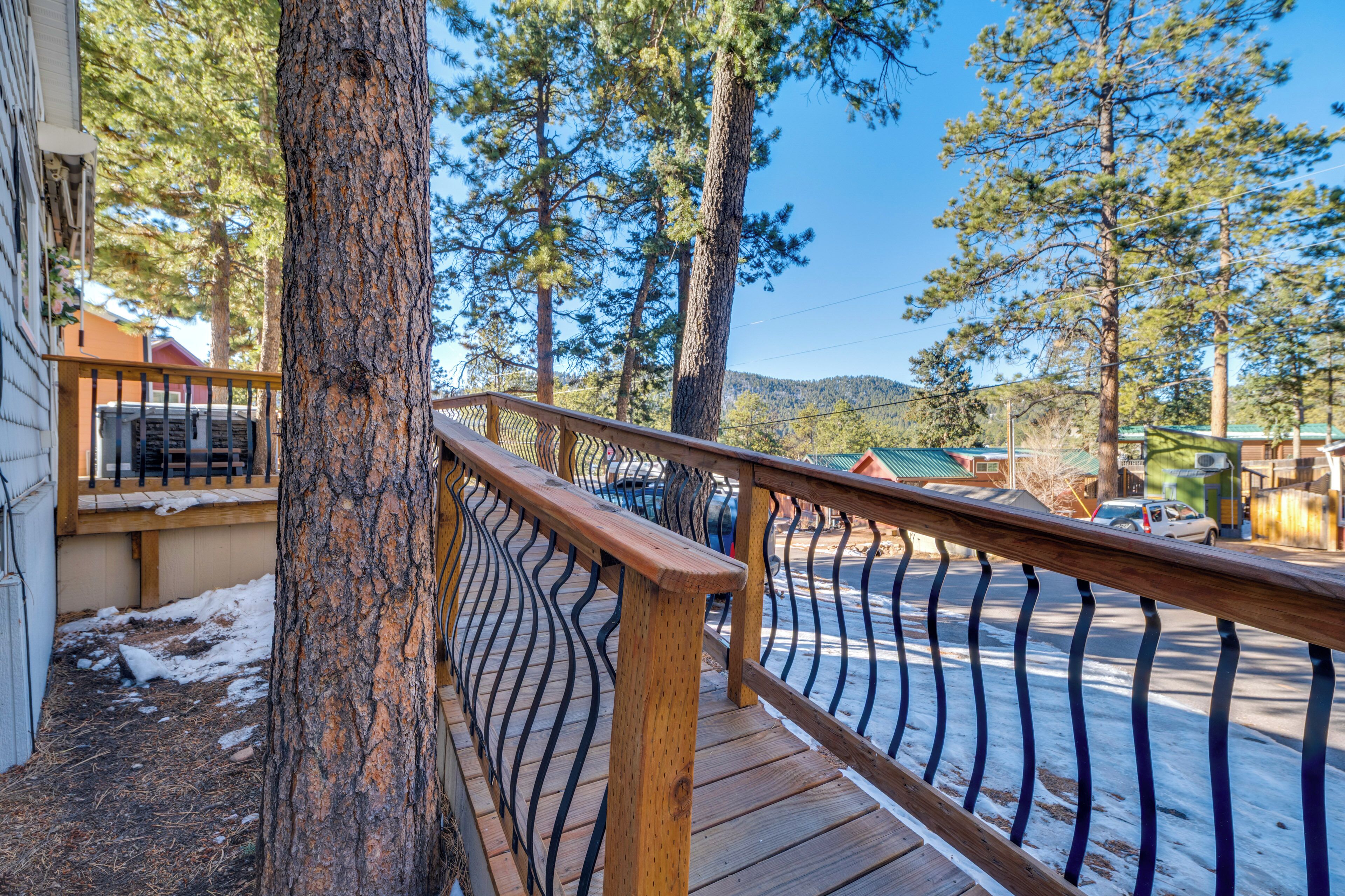 A wooden deck with a metal railing overlooking a snowy street and a residential area with houses and trees.