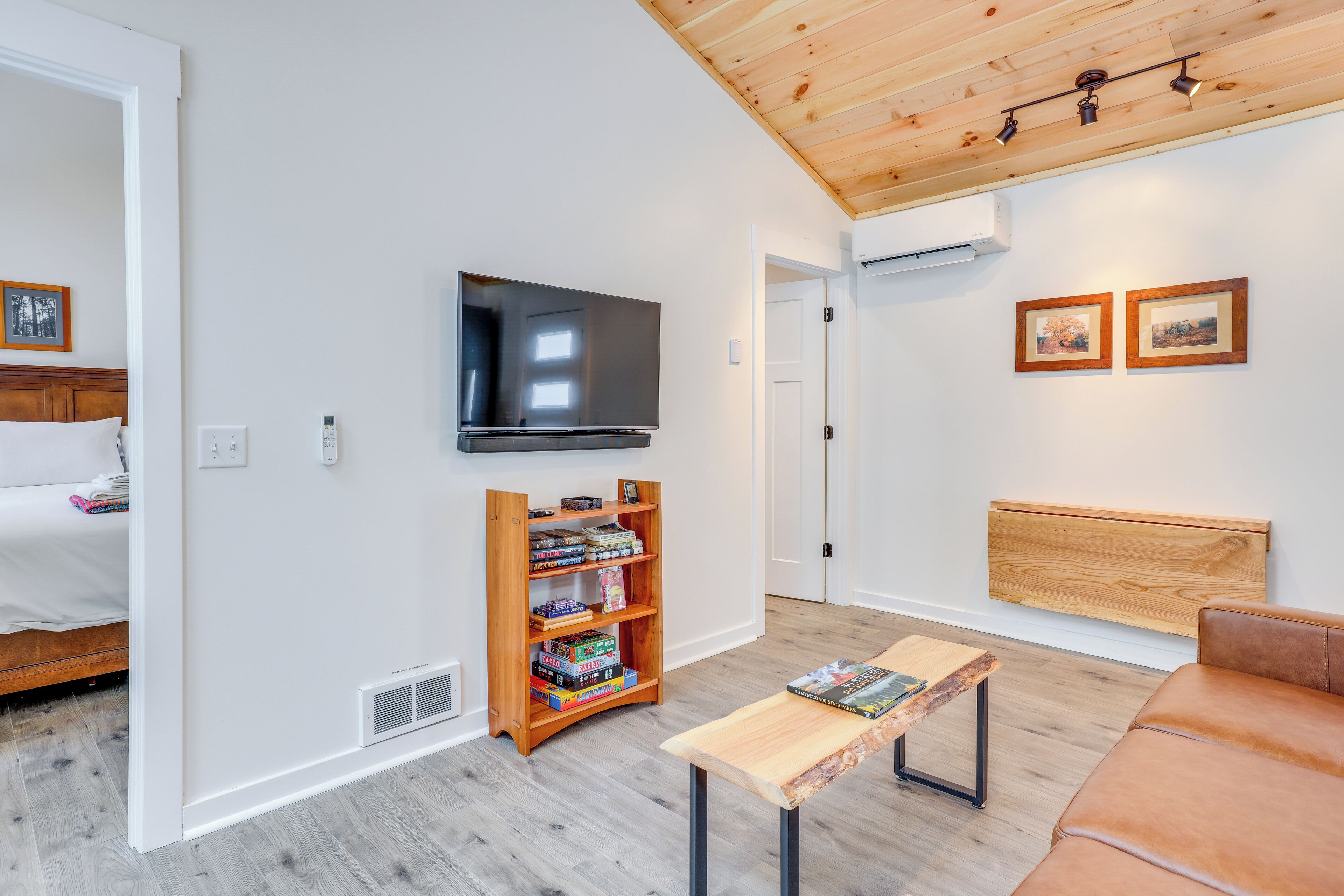 A modern living room with a flat-screen TV, wooden bookshelf, and a brown leather couch.