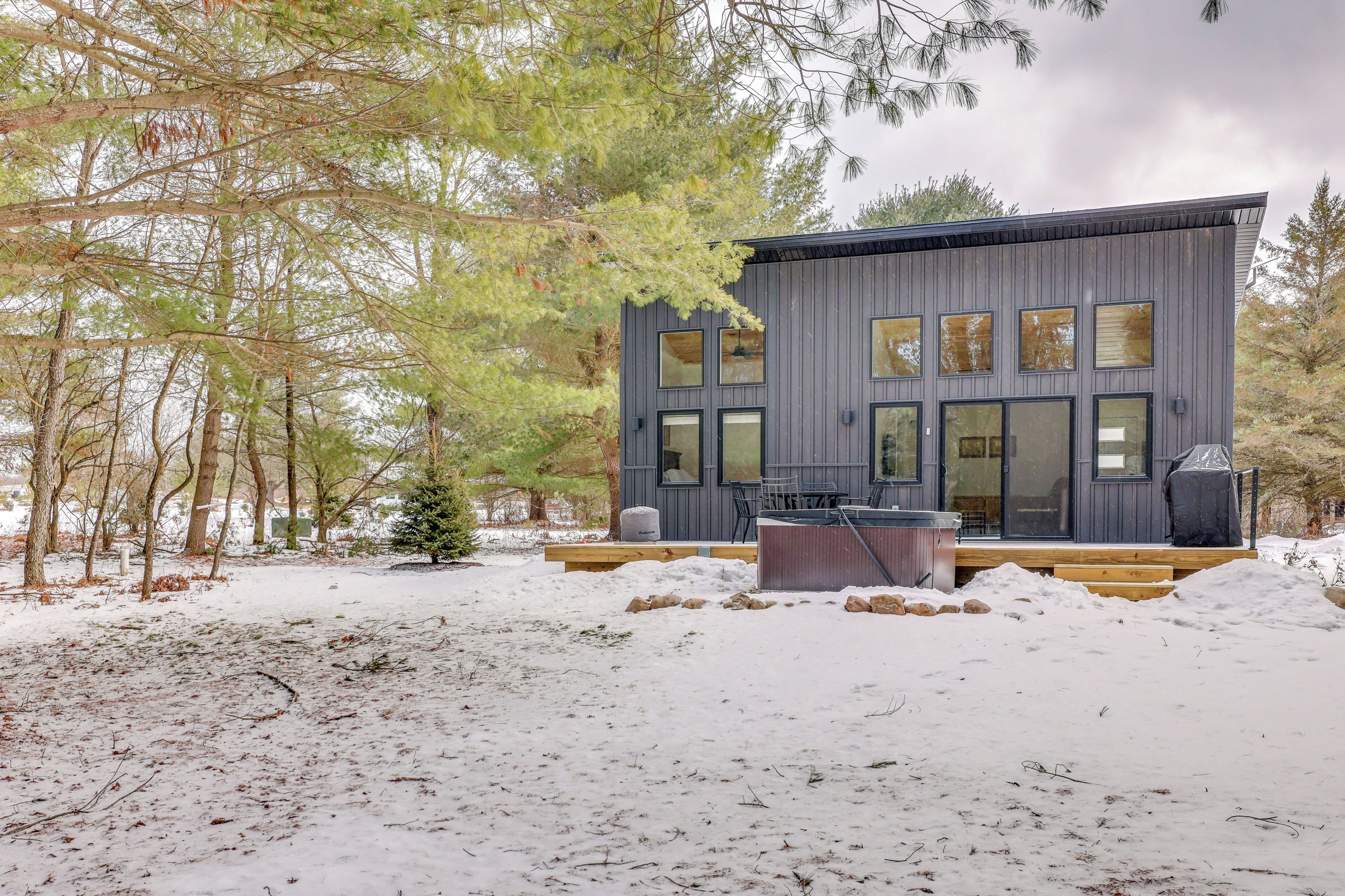 A modern house with a deck, surrounded by trees and snow.
