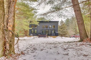 Une cabane moderne dotée d’une terrasse, entourée d’arbres et de neige.