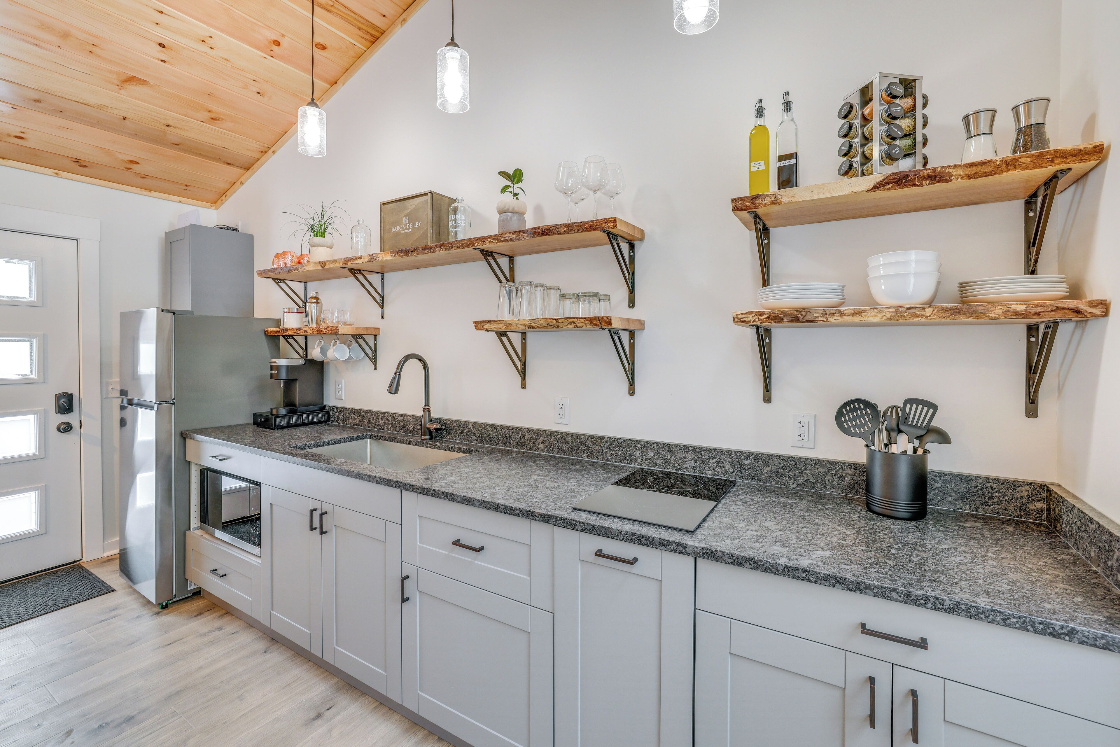 A modern kitchen with granite countertops, stainless steel appliances, and wooden shelves with kitchenware.