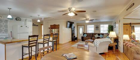 A spacious living area with a wooden dining table, a kitchen with white appliances, and a cozy seating area with a sofa and armchairs.