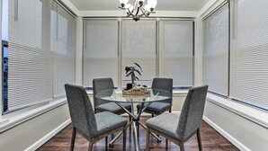 A dining area with a glass table, four grey chairs, a chandelier, and a decorative plant. - Pet-friendly Newark Townhome Near Airport! (Newark)