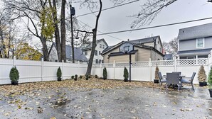 A backyard with a concrete patio, a basketball hoop, a white fence, and potted plants. - Pet-friendly Newark Townhome Near Airport! (Newark)