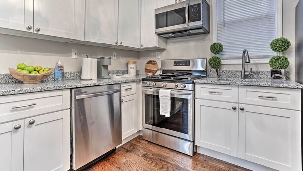 A modern kitchen with white cabinets, stainless steel appliances, a microwave, a stove, and a dishwasher. - Pet-friendly Newark Townhome Near Airport! (Newark)