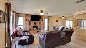 Un salón acogedor con chimenea, sofá de cuero y zona de comedor con una cocina al fondo.