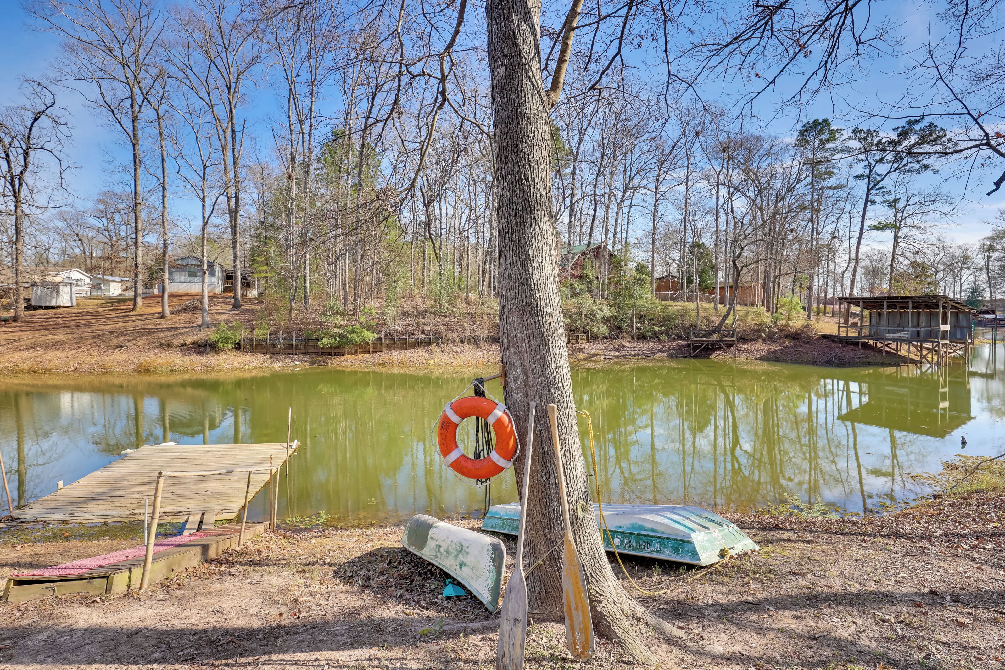 A wooden dock extending into a calm pond surrounded by trees and a small building.