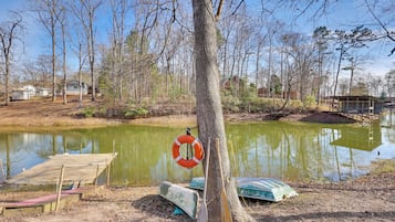 A wooden dock extending into a calm pond surrounded by trees and a small building.