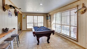 Una mesa de billar en una sala con paredes de madera, una ventana con persianas y un dardo.