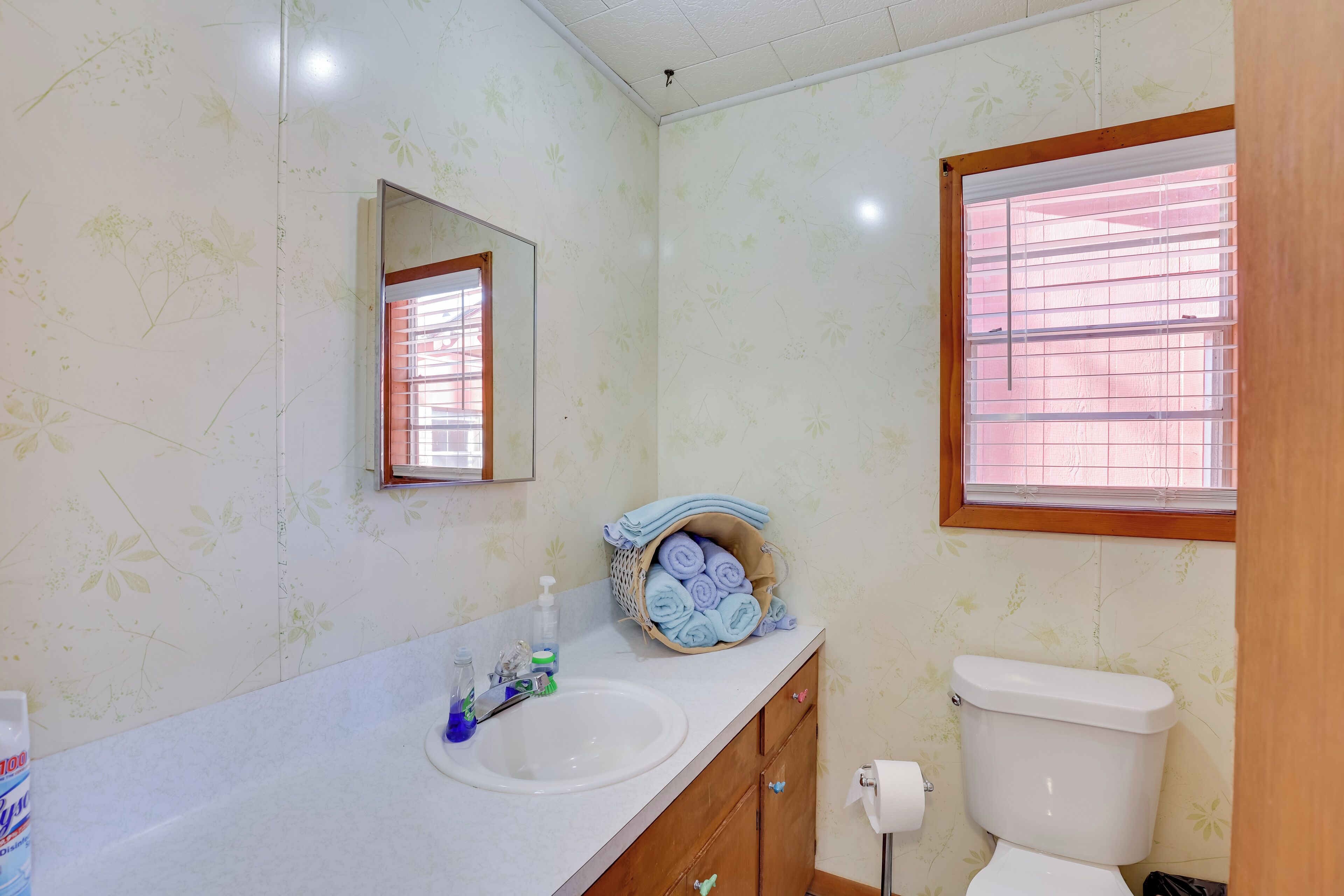 Ein Badezimmer mit Waschbecken, Spiegel, Toilette und einem Fenster mit Jalousien.