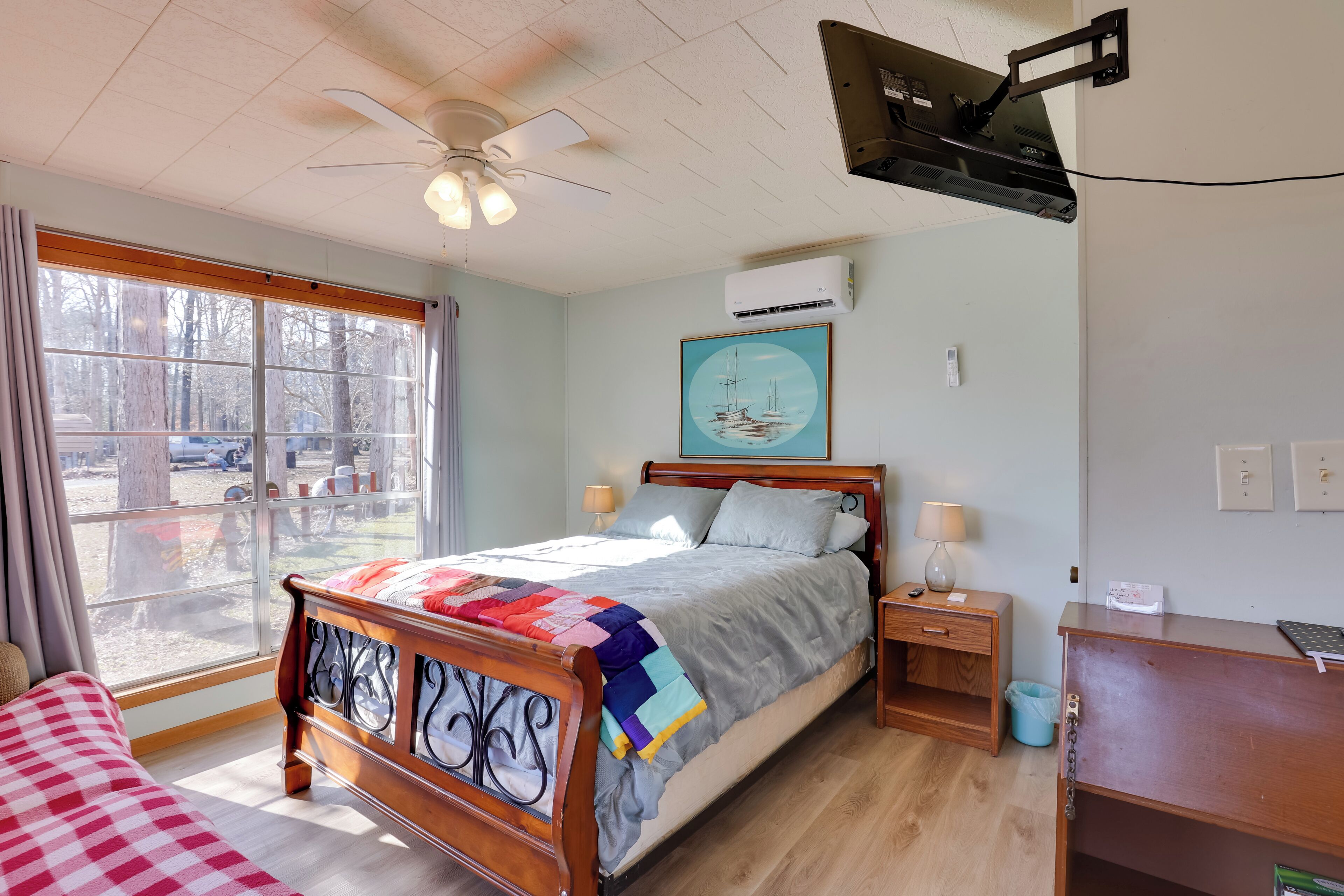 Ein Schlafzimmer mit Bett, Schreibtisch, Stuhl, Fenster und Deckenventilator.