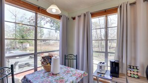 A cozy room with large windows, a table with a floral tablecloth, a basket, a coffee maker, and a tray of coffee pods. - Great for Fishing! Lakefront Studio in Hemphill (Hemphill)