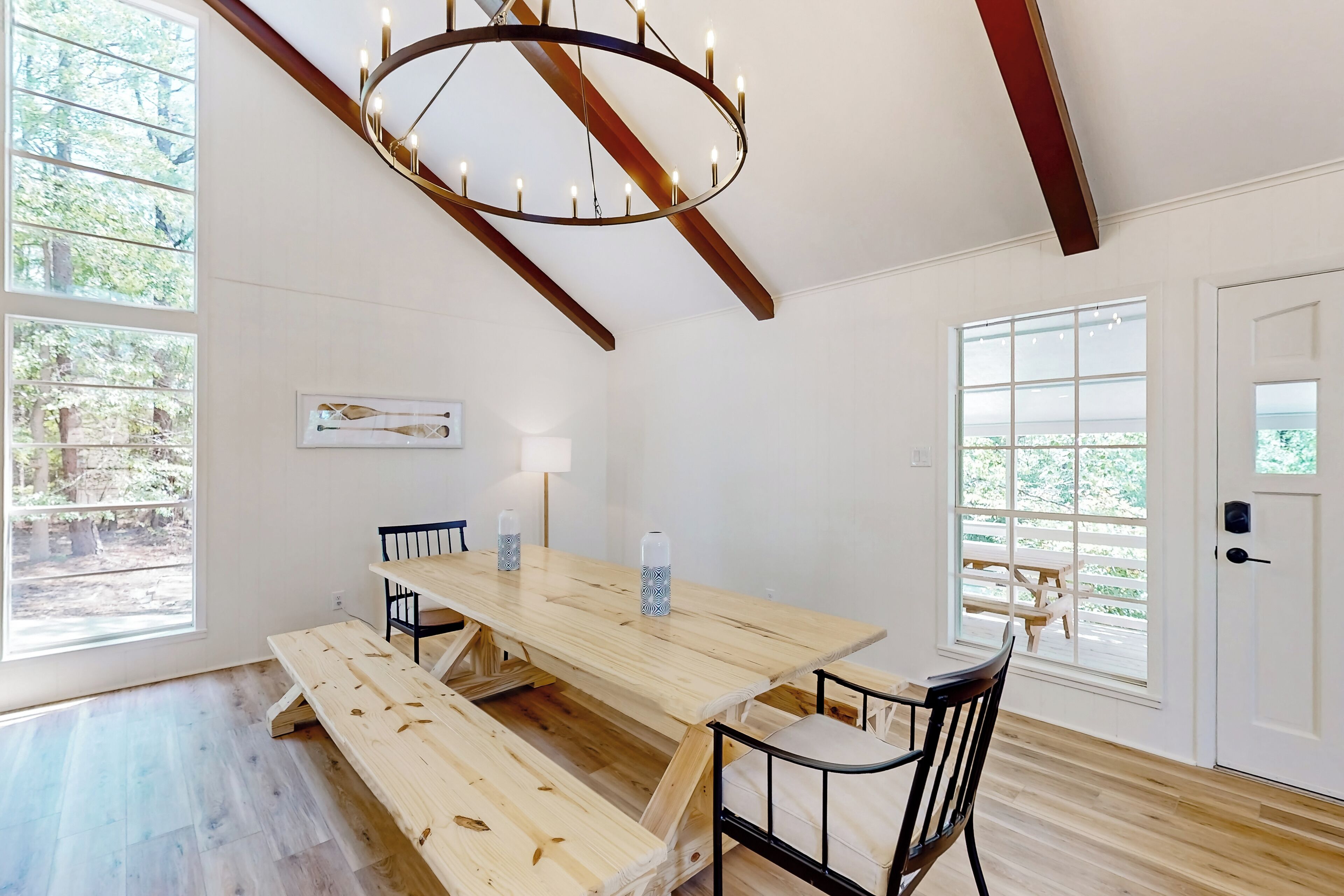A spacious dining area with a wooden table and benches, large windows with views of greenery, and a modern chandelier.