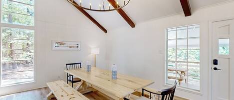 A spacious dining area with a wooden table and benches, large windows with views of greenery, and a modern chandelier.