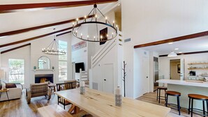A spacious living room with a large wooden table, a chandelier, and a staircase leading to an upper level. - Modern Treehouse Vibes Close to Club and Lake (Brookeland)