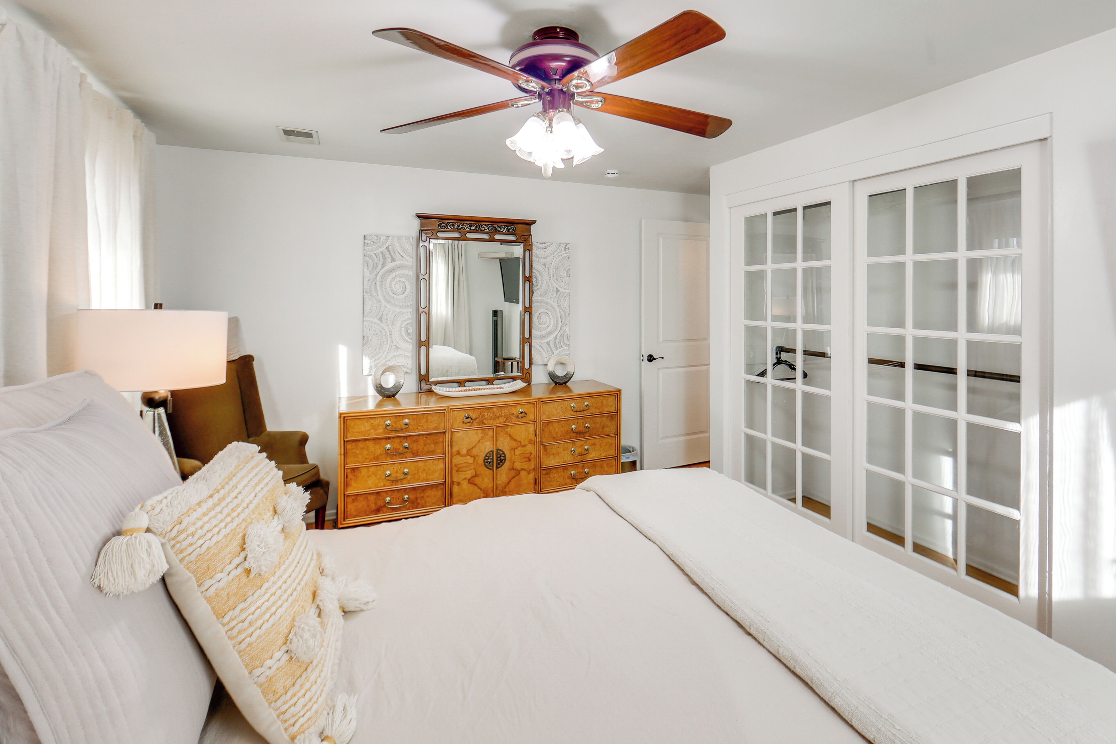A bedroom with a bed, a dresser, a mirror, a ceiling fan, and a sliding glass door.