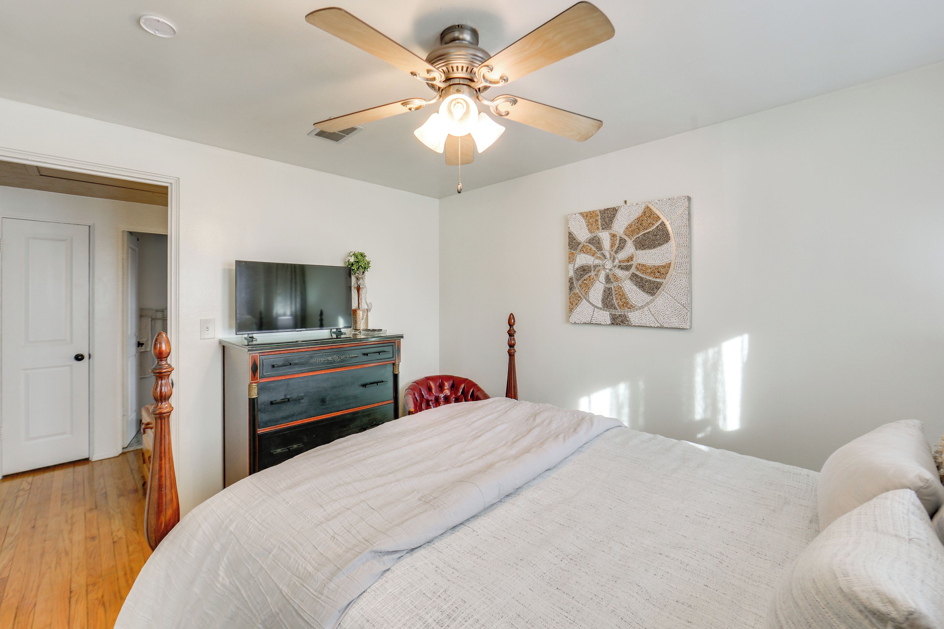 A bedroom with a bed, a dresser, a television, and a ceiling fan.