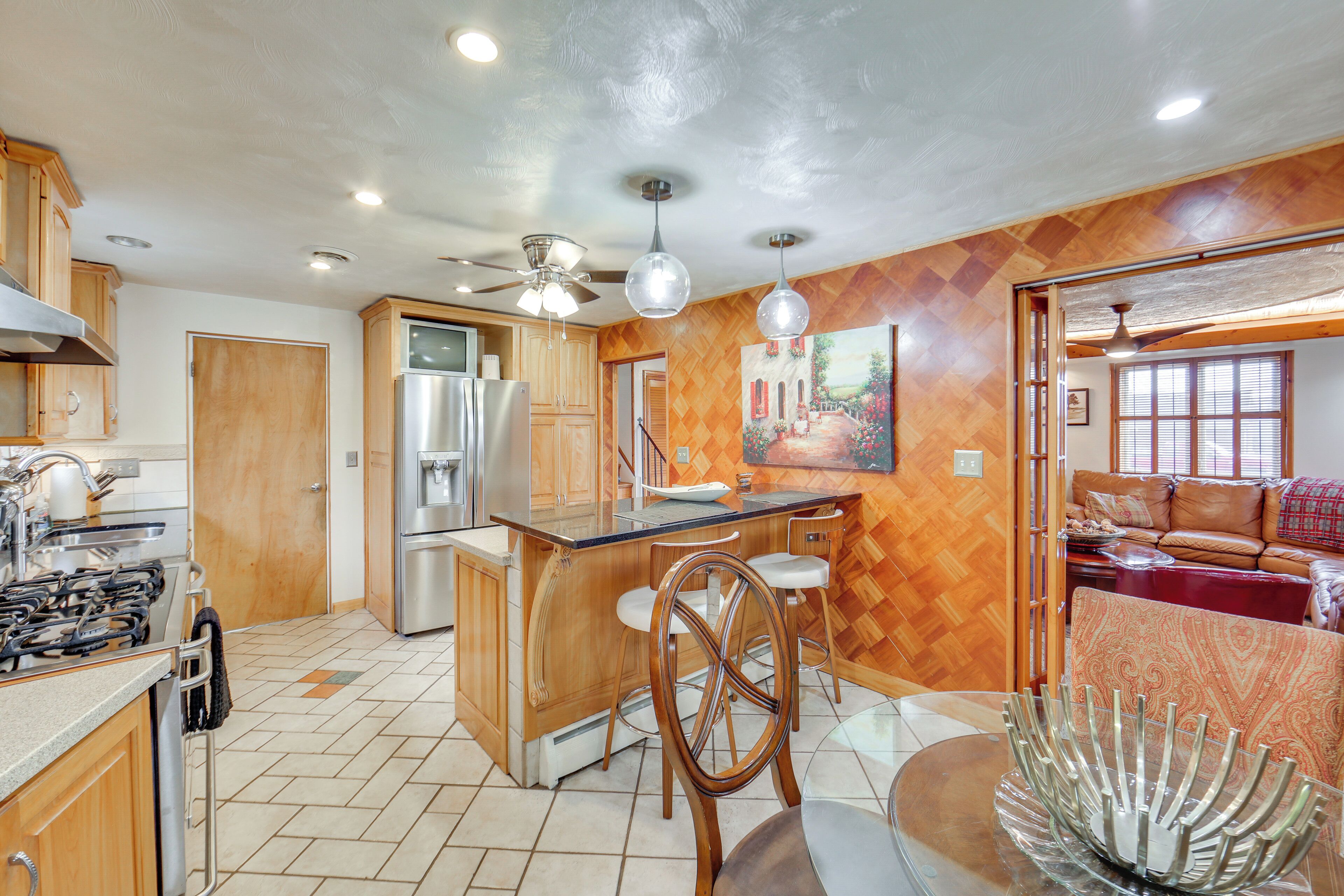 A kitchen with wooden cabinets, a stainless steel refrigerator, a bar area, and a dining table with chairs.