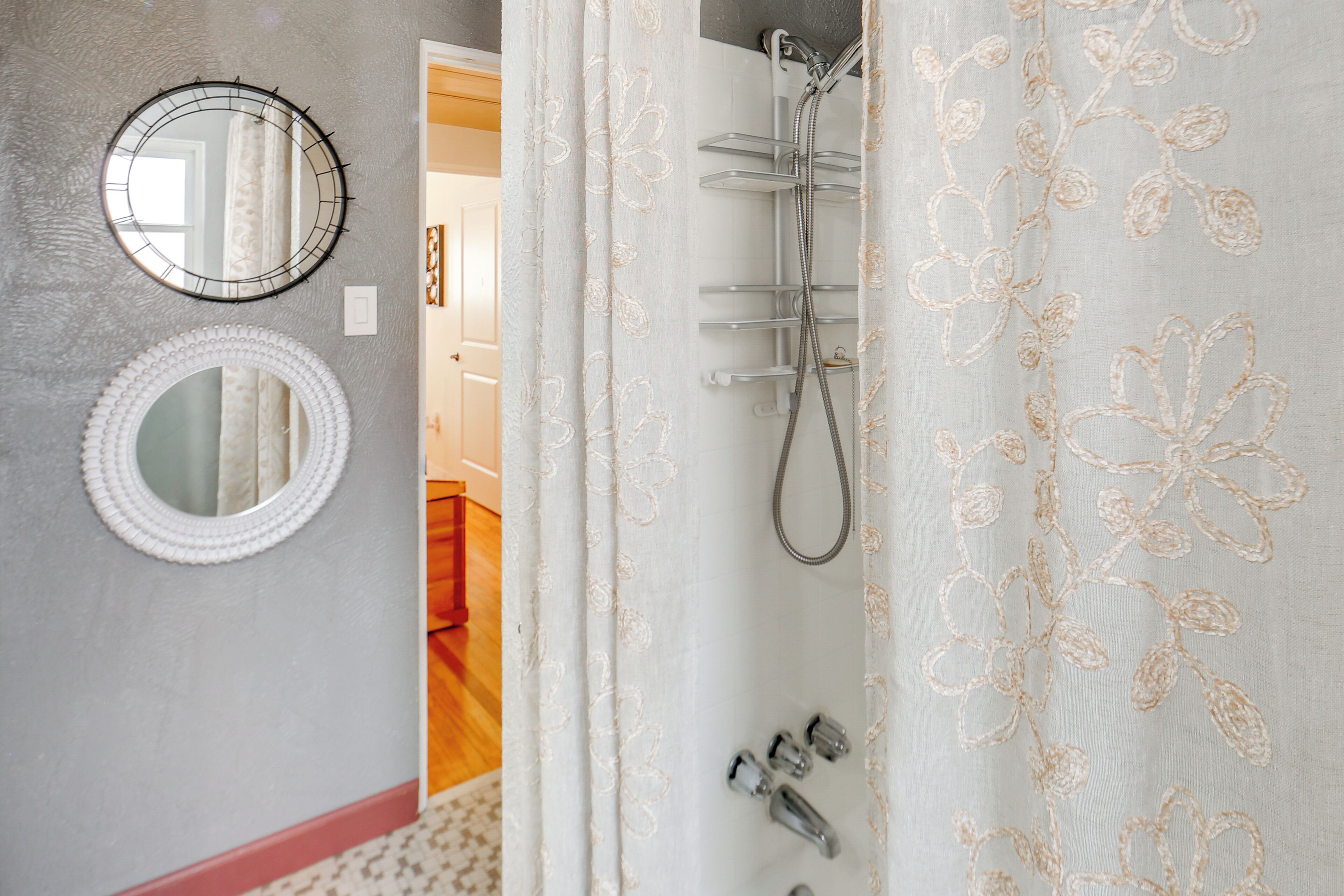 A bathroom with a shower, two round mirrors, and a curtain with floral embroidery.