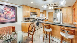 A modern kitchen with wooden cabinets, stainless steel appliances, a bar area, and a ceiling fan.
