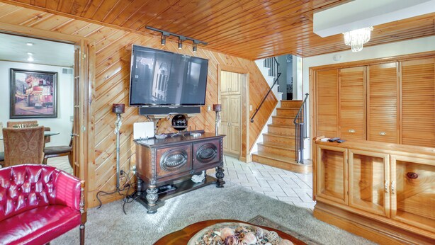 A living room with a wooden ceiling, a television on a wooden stand, a red leather sofa, a wooden cabinet, and a staircase.