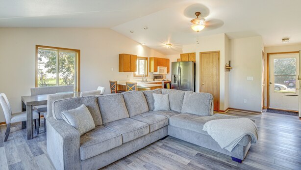 A modern living room with a sectional sofa, a dining area with a table and chairs, a kitchen with wooden cabinets, and a large window providing natural light. - Angler's Retreat 1 Block to Lake Winneconne (Winneconne)