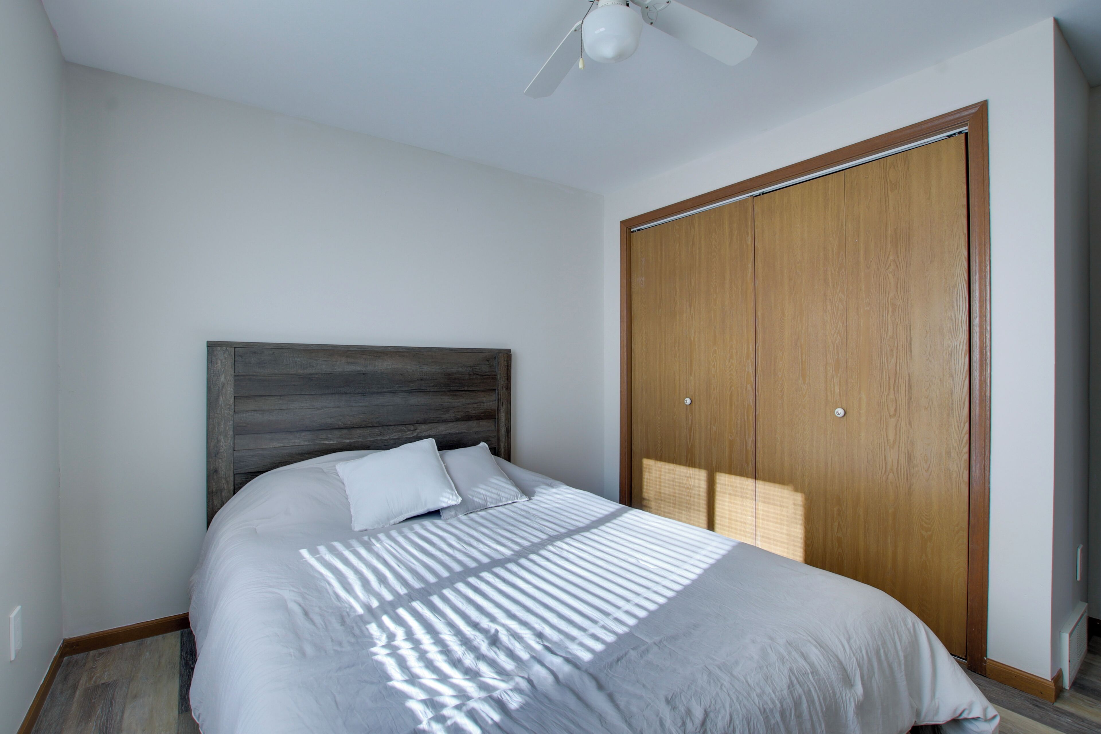 A bedroom with a bed, a wooden headboard, a wardrobe, and a ceiling fan.