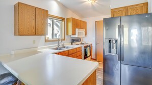 A modern kitchen with wooden cabinets, a stainless steel refrigerator, a built-in oven, and a large island. - Angler's Retreat 1 Block to Lake Winneconne (Winneconne)