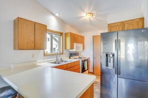 A modern kitchen with wooden cabinets, a stainless steel refrigerator, and a built-in oven. - Angler's Retreat 1 Block to Lake Winneconne (Winneconne)