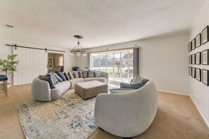 A spacious living room with a sectional sofa, a round armchair, and a large window providing a view of the outdoors.