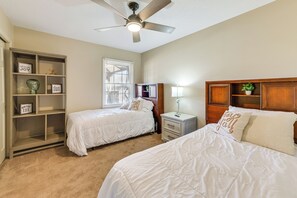 A bedroom with two beds, a ceiling fan, a nightstand with a lamp, a bookshelf, and a window with blinds. - Walk to Town Square! Georgia Small-town Getaway (Buena Vista)
