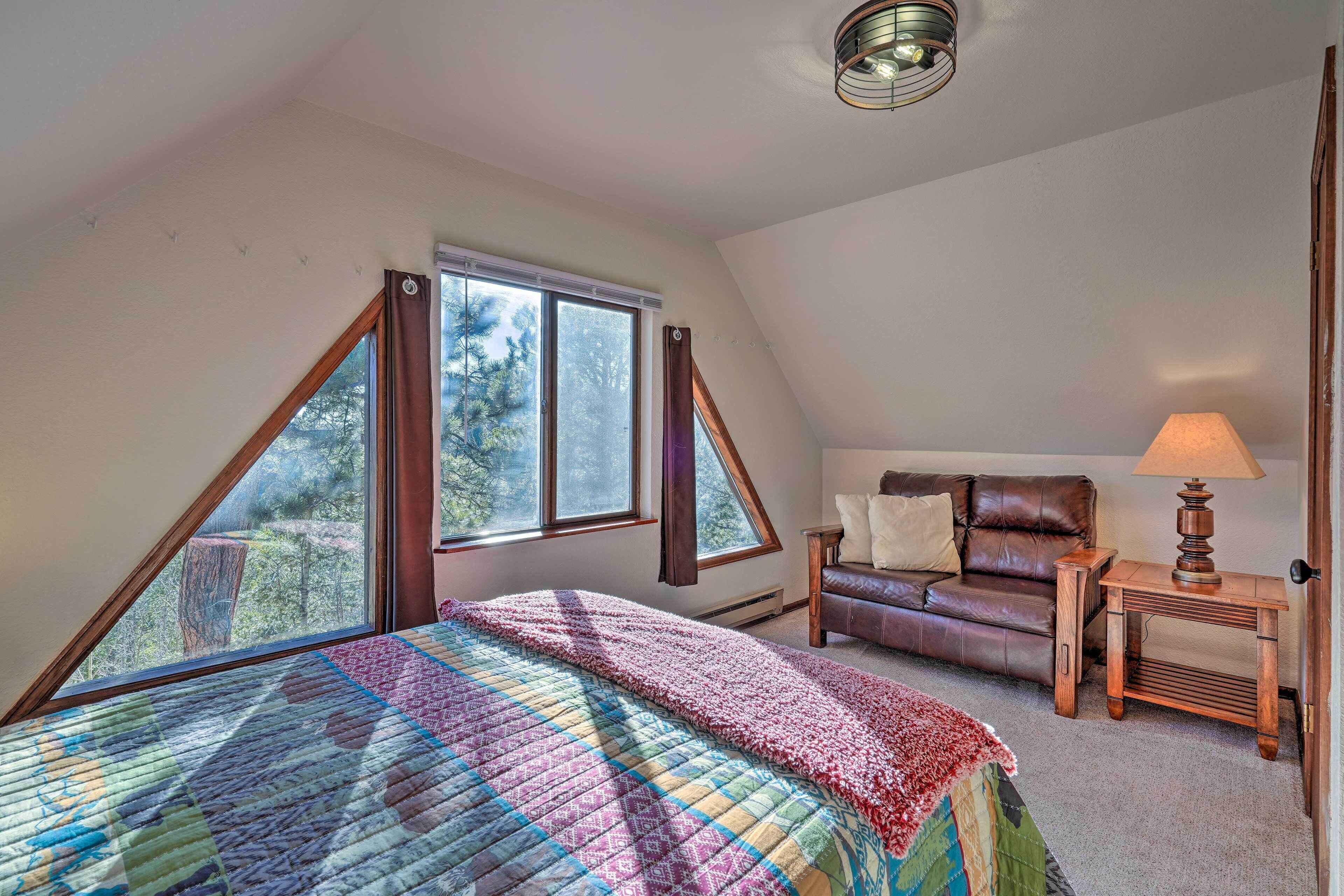 Een slaapkamer met een groot bed, een houten nachtkastje, een leren bank en een raam met uitzicht op bomen.