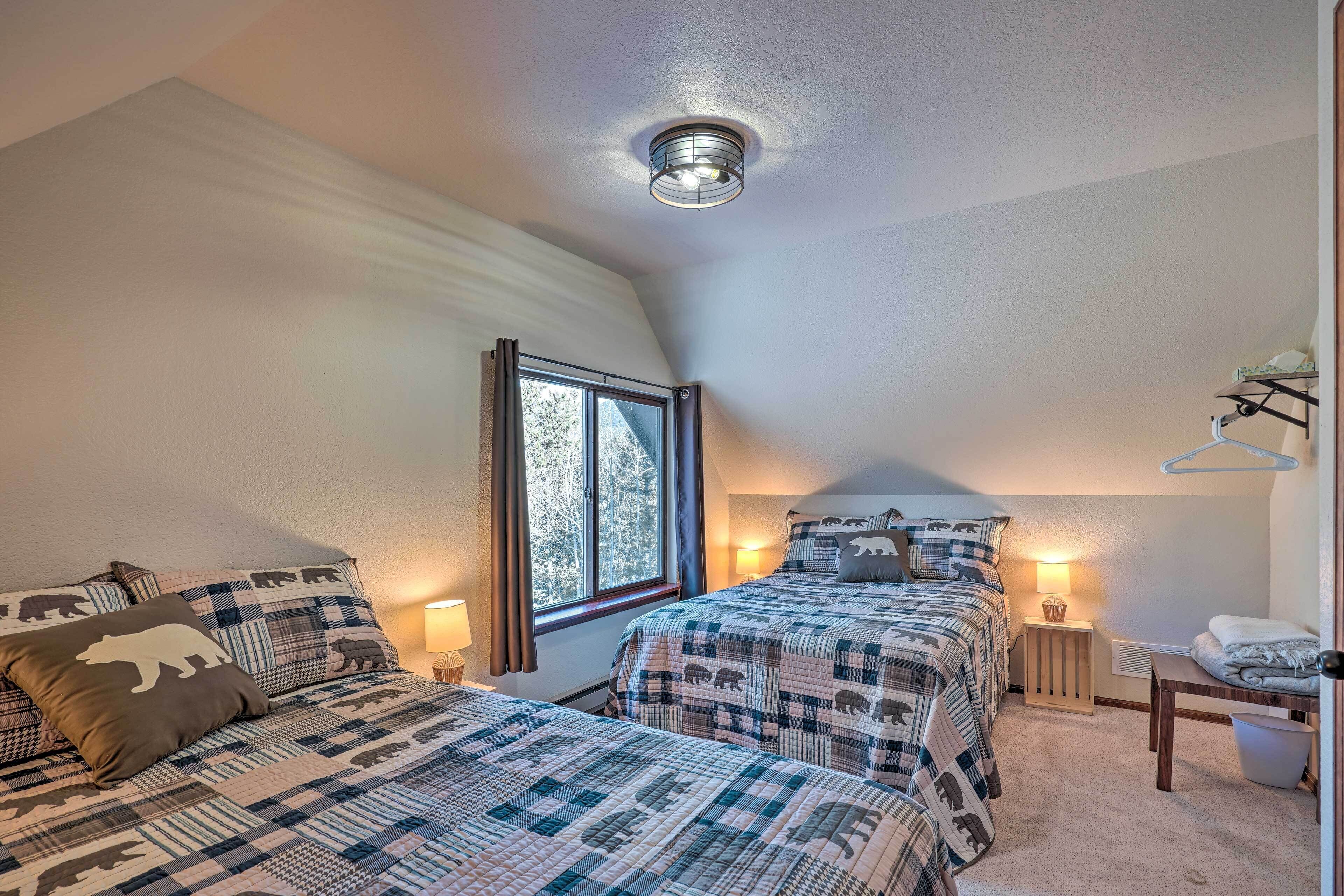 A bedroom with two beds, a window, a ceiling light, and a bedside table with a lamp.