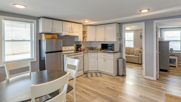 A modern kitchen with white cabinets, stainless steel appliances, and a dining area with a table and chairs. - Walk to Public Beach Access! Breezy Hampton Condo (Hampton)