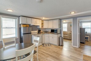 A modern kitchen with white cabinets, stainless steel appliances, and a dining area with a table and chairs. - Walk to Public Beach Access! Breezy Hampton Condo (Hampton)