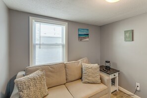 A living room with a beige sofa, a small table with a lamp, and a window with blinds. - Walk to Public Beach Access! Breezy Hampton Condo (Hampton)