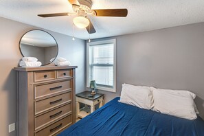 A bedroom with a bed, a dresser, a mirror, a ceiling fan, and a window. - Walk to Public Beach Access! Breezy Hampton Condo (Hampton)