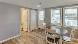 A dining area with a round table and four chairs, a door leading to a bathroom, and a window with blinds. - Walk to Public Beach Access! Breezy Hampton Condo (Hampton)