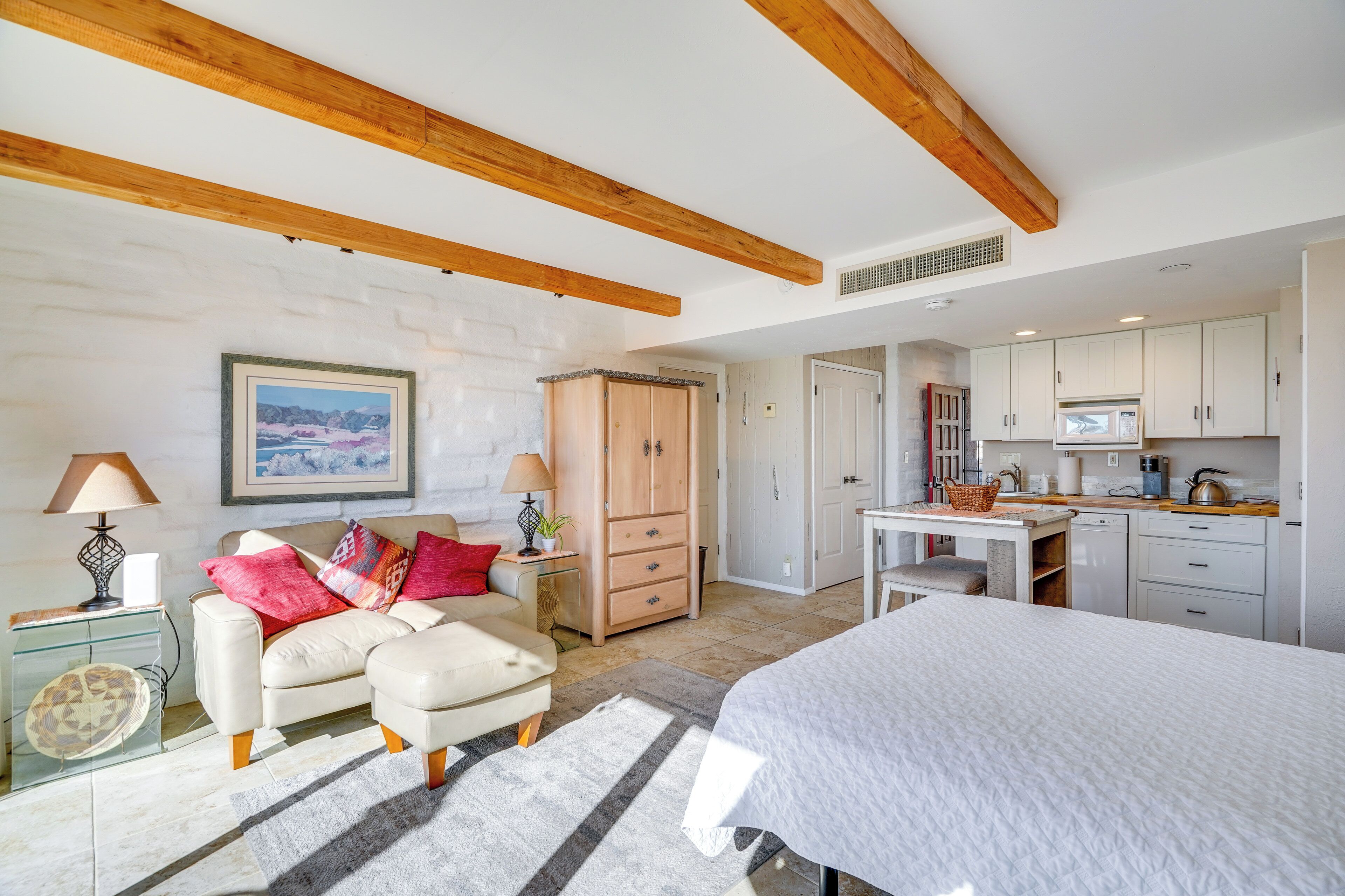 Un dormitorio moderno con una cama grande, un sofá y un escritorio. Hay una zona de cocina con armarios y un microondas.